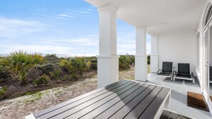 A covered outdoor area with a wooden deck, two chairs, and a table. - GULF-FRONT 3BR Condo! Steps to Beach & Community Pool! (Seacrest)