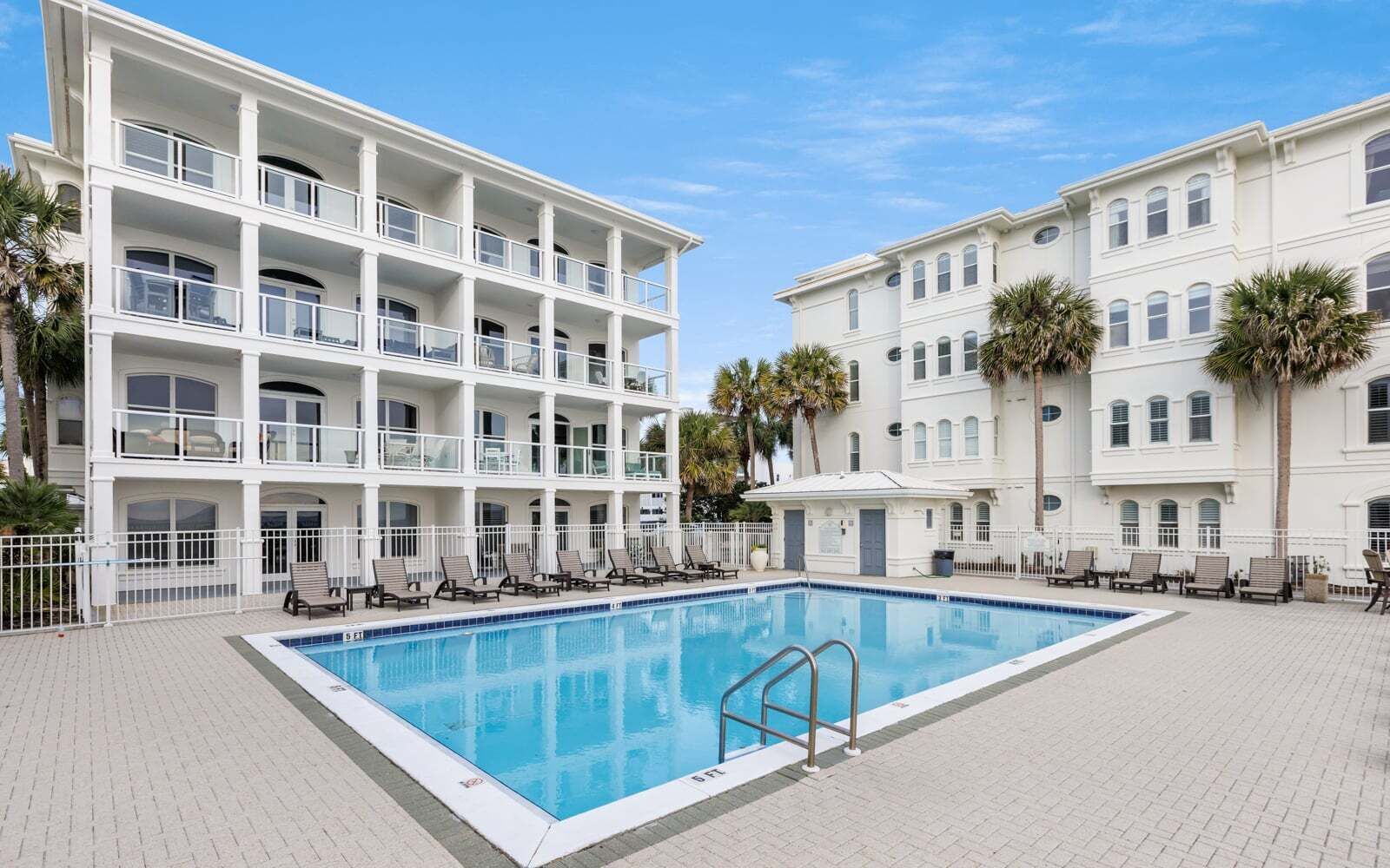 A multi-story hotel with a pool area, including lounge chairs and a clear blue pool.