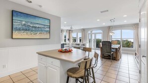 A spacious kitchen with a large island, a dining area with a table and chairs, and a view through large windows. - GULF-FRONT 3BR Condo! Steps to Beach & Community Pool! (Seacrest)