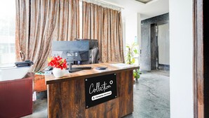 A reception desk with a sign reading 'Collection & Company-Serviced,' a computer, a printer, and a vase with flowers. - Deluxe Super Collection O Banaswadi (Bengaluru)