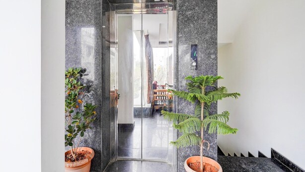 A modern elevator with glass doors, a marble wall, and potted plants on either side. - Deluxe Super Collection O Banaswadi (Bengaluru)