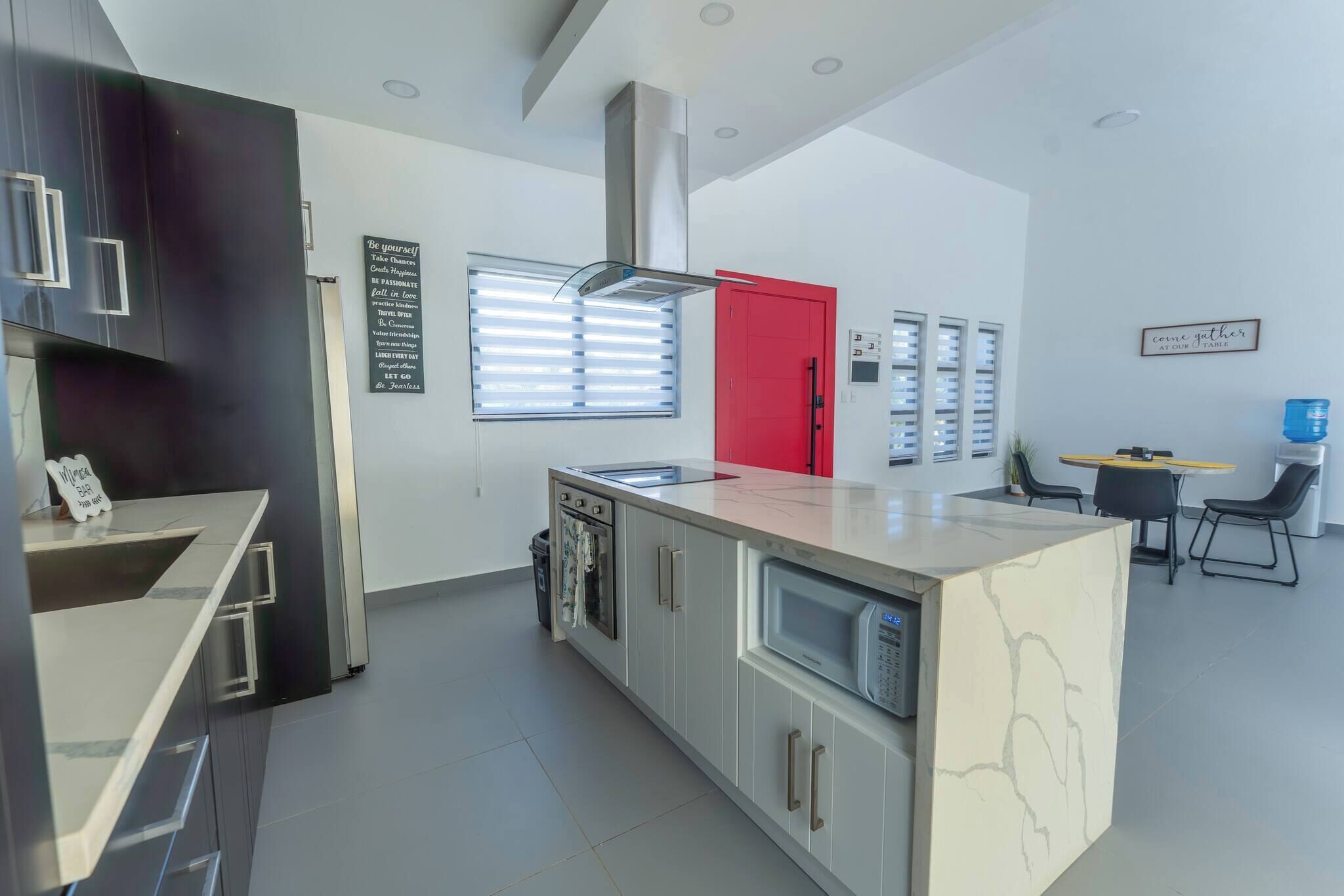 A modern kitchen with a central island, built-in oven, and a red door.