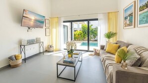 Una sala de estar con televisión, un sofá, una mesa de centro y vista a una piscina.