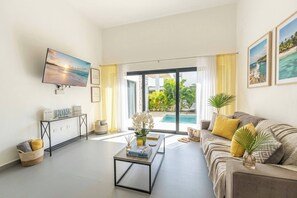 A living room with a TV, a sofa, a coffee table, and a view of a swimming pool. - Modern Luxury Villa in Sosua Ocean Village (Sosúa)