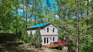 A two-story cabin with a deck, surrounded by dense forest.