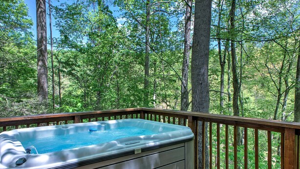 A hot tub on a wooden deck with a forest backdrop.
