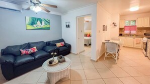 Uma sala de estar com um sofá de couro preto, uma mesa de centro redonda de vime e um ventilador de teto.