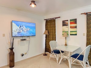 A room with a television on the wall, a dining table with chairs, a lamp, and a vase with plants. - Garden Condos APT 44 - Comfy 1BR APT in Sosua! (Sosúa)