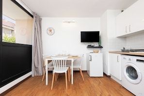A compact kitchen with a dining area, a washing machine, a television, and a clock on the wall. - Upstays charming t2 renovated balcony and  pool (Cannes)
