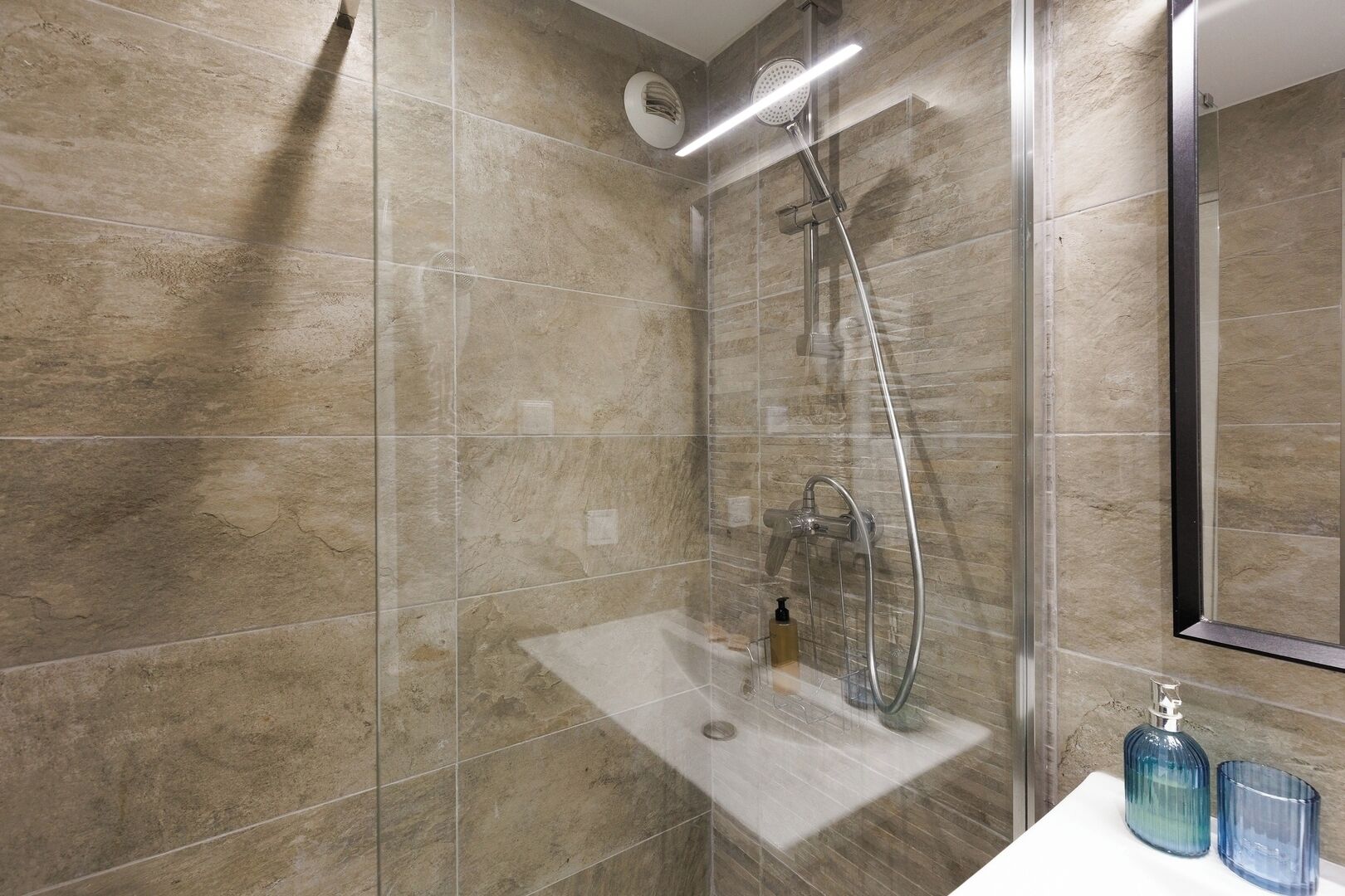 Un baño moderno con ducha envuelta en vidrio, un lavamanos blanco y un espejo.