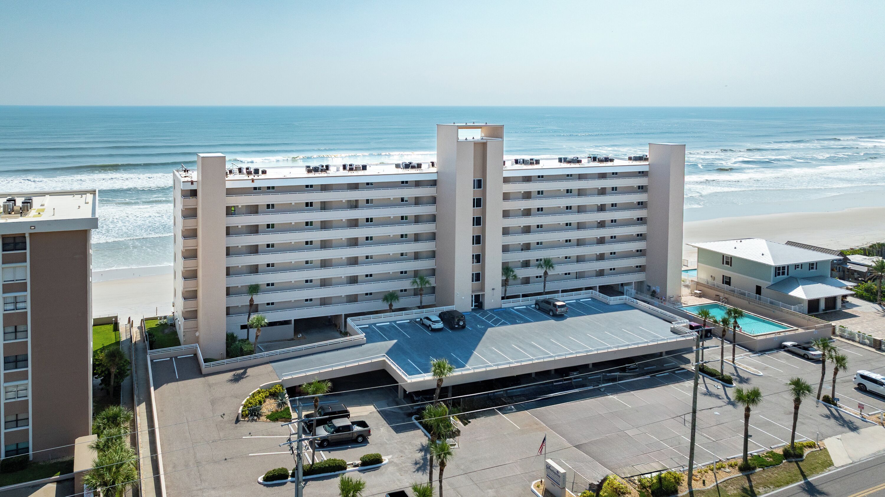 A multi-story hotel with a rooftop pool, parking area, and ocean view.