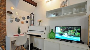 Ein gemütlicher Wohnraum mit Klavier, Fernseher und verschiedenen Wandbildern.