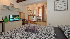 Ein Hotelzimmer mit Bett, Fernseher, einer grünen Vase, einem Schreibtisch und einer Küchenzeile.