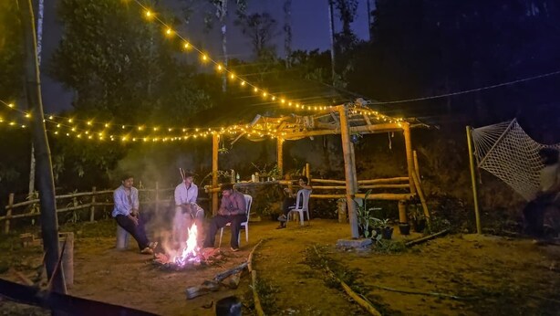 A rustic outdoor setting with a wooden pergola, string lights, and a fire pit.