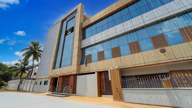 Un edificio moderno con amplias ventanas, una entrada destacada y un camino de acceso con puerta de reja.