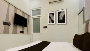 Et hotelværelse med en seng, et vægmonteret fladskærms-TV, et vindue og to billeder af blade på væggen.
