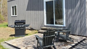 A house with a patio area featuring a grill, outdoor seating, and a large window.