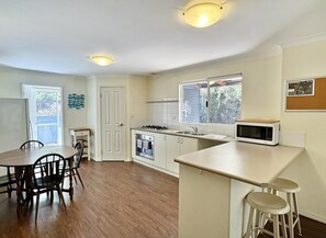 A compact kitchen with a dining area, white cabinetry, a stove, and a microwave.