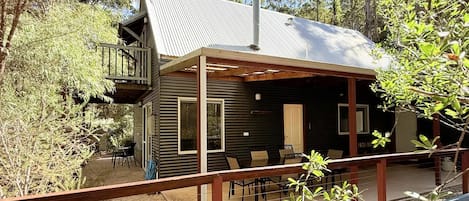 A cabin with a balcony, a covered patio, and a view of the surrounding forest.
