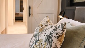 Una cama con almohadas estampadas con motivos florales, una puerta y una lámpara en una habitación.