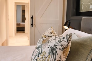 Un lit avec des oreillers à motifs floraux, une porte et une lampe dans une pièce.