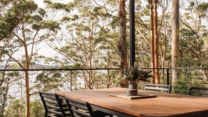 Una terraza de madera con una mesa y sillas, con vistas a un área boscosa y al agua.