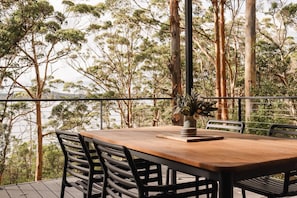 Une terrasse en bois avec une table et des chaises, donnant sur une zone boisée et offrant une vue sur l’eau.