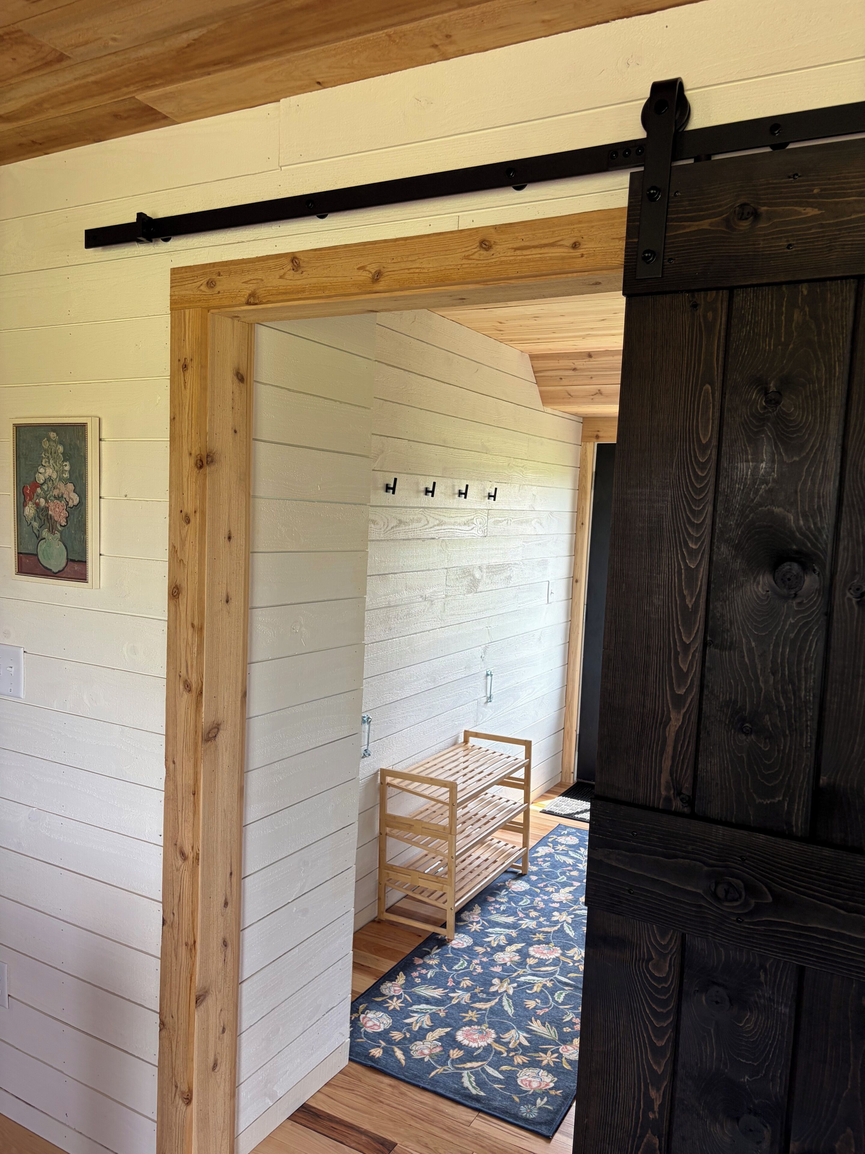 A hallway with wooden walls, a wooden bench, a dark wooden door, and a patterned rug.