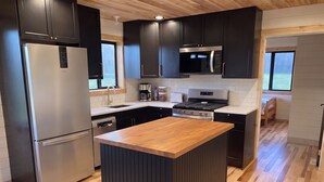 Cocina moderna con armarios oscuros, electrodomésticos de acero inoxidable, una isla de madera y vistas al exterior.