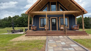 Una cabaña de madera con un porche, una parrilla y un camino de piedra que lleva a la entrada.