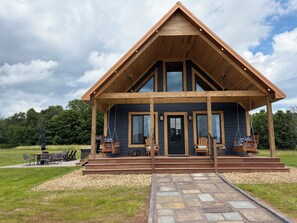 A wooden cabin with a porch, a grill, and a stone pathway leading to the entrance.