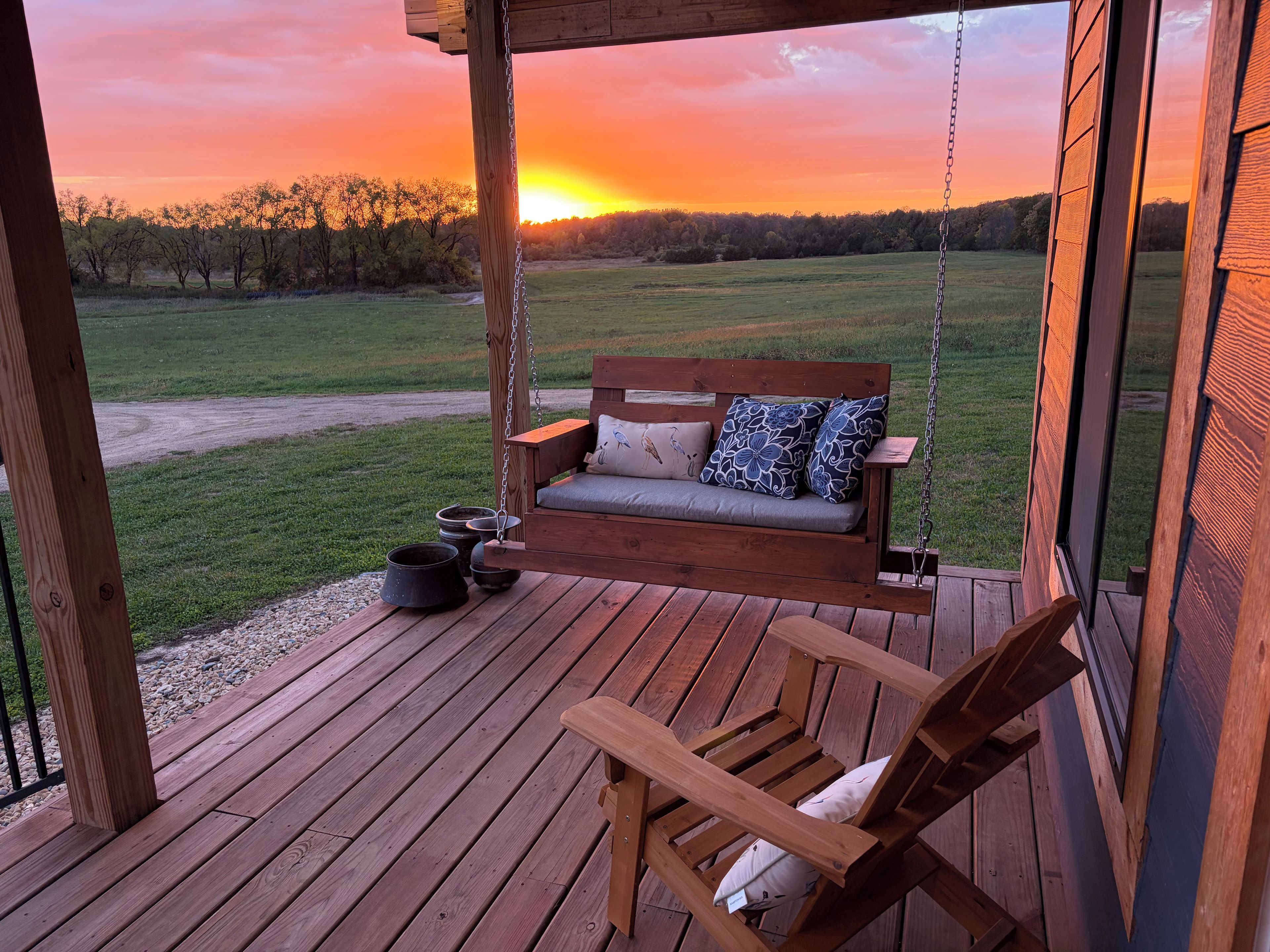 A wooden deck with a swing chair and a bench with cushions.