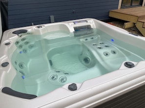 A hot tub with multiple jets, a control panel, and a wooden deck in the background.