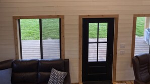 Habitación estilo loft con techo inclinado, ventanas amplias, un sofá de cuero oscuro y una puerta de madera.
