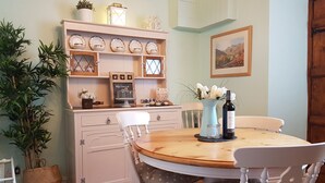 Un comedor con una mesa redonda de madera, sillas blancas, un aparador blanco con objetos decorativos y un cuadro en la pared.