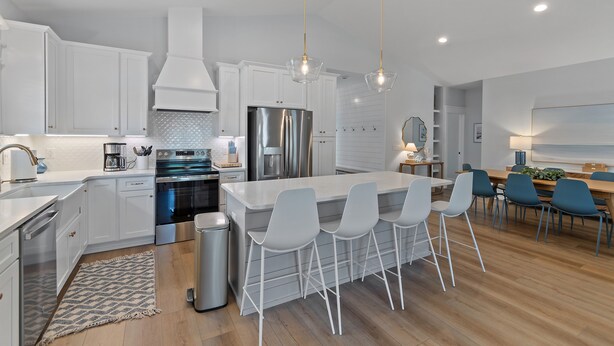 Una cocina moderna con armarios blancos, electrodomésticos de acero inoxidable y una isla central con taburetes de bar.