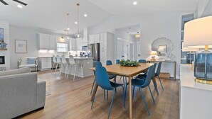 Una cocina moderna con armarios blancos, una isla central y sillas azules alrededor de una mesa de comedor de madera.