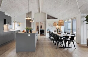 A spacious kitchen with a central island, pendant lighting, and a dining area with a long table and chairs. - Nice home in Otterup with sauna (Otterup)