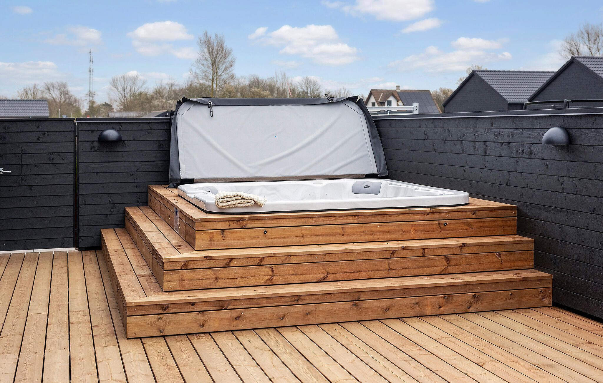 A hot tub on a wooden deck with a covered top, surrounded by a dark wooden fence.