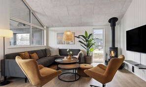 A cozy living room with a sectional sofa, a round coffee table, two armchairs, a TV, a fireplace, and a large window. - Nice home in Otterup with sauna (Otterup)
