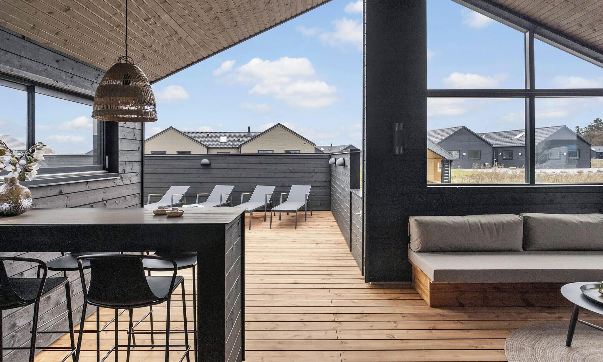 Una terraza moderna en la azotea con cubierta de madera, zona de bar, sillones de descanso y un sofá.
