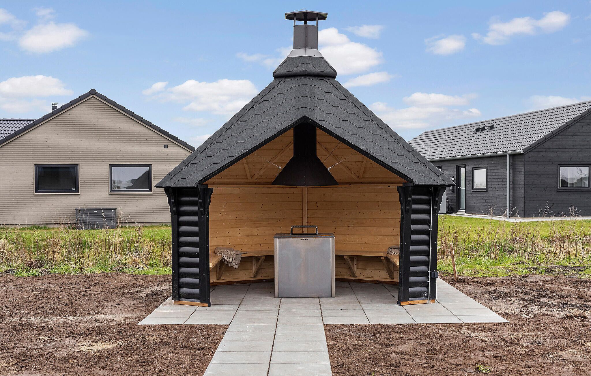 A modern outdoor fireplace structure with a sloped roof and chimney, surrounded by a paved area.
