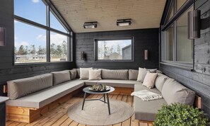 A modern interior with a sectional sofa, a round table, and large windows offering a view of the outdoors. - Nice home in Otterup with sauna (Otterup)