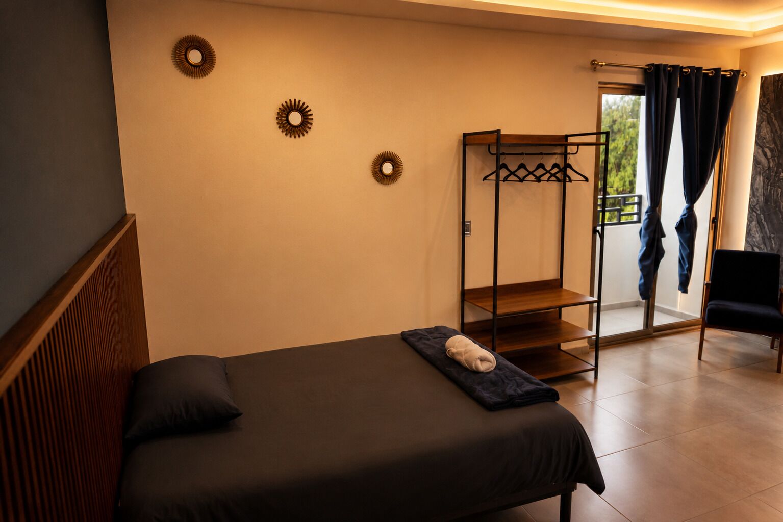 A bedroom with a bed, a wooden bench, a coat rack, and a view of the outdoors.