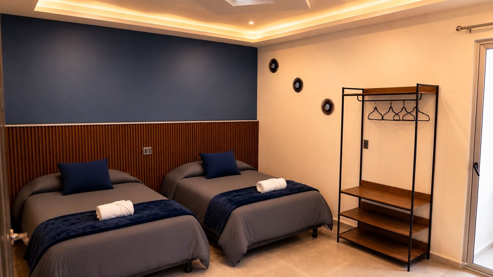 A hotel room with two beds, a wooden headboard, a coat rack, and a door.