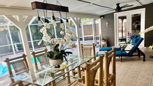 Ein Tisch mit Glasplatte, Bambusstühle, ein Topf mit Pflanze und Blick auf einen Swimmingpool.
