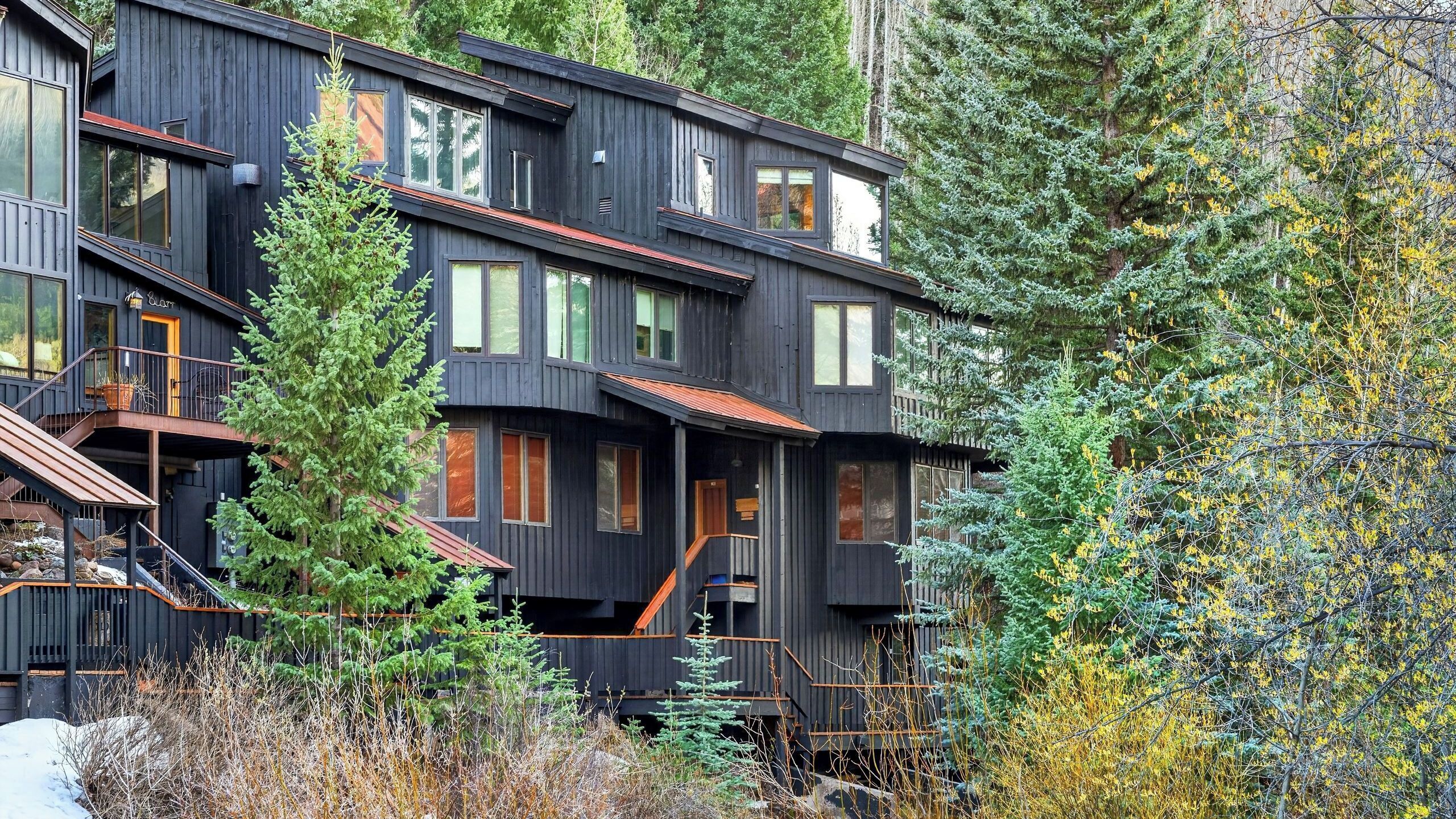 A multi-story wooden building with balconies, surrounded by trees and shrubs.