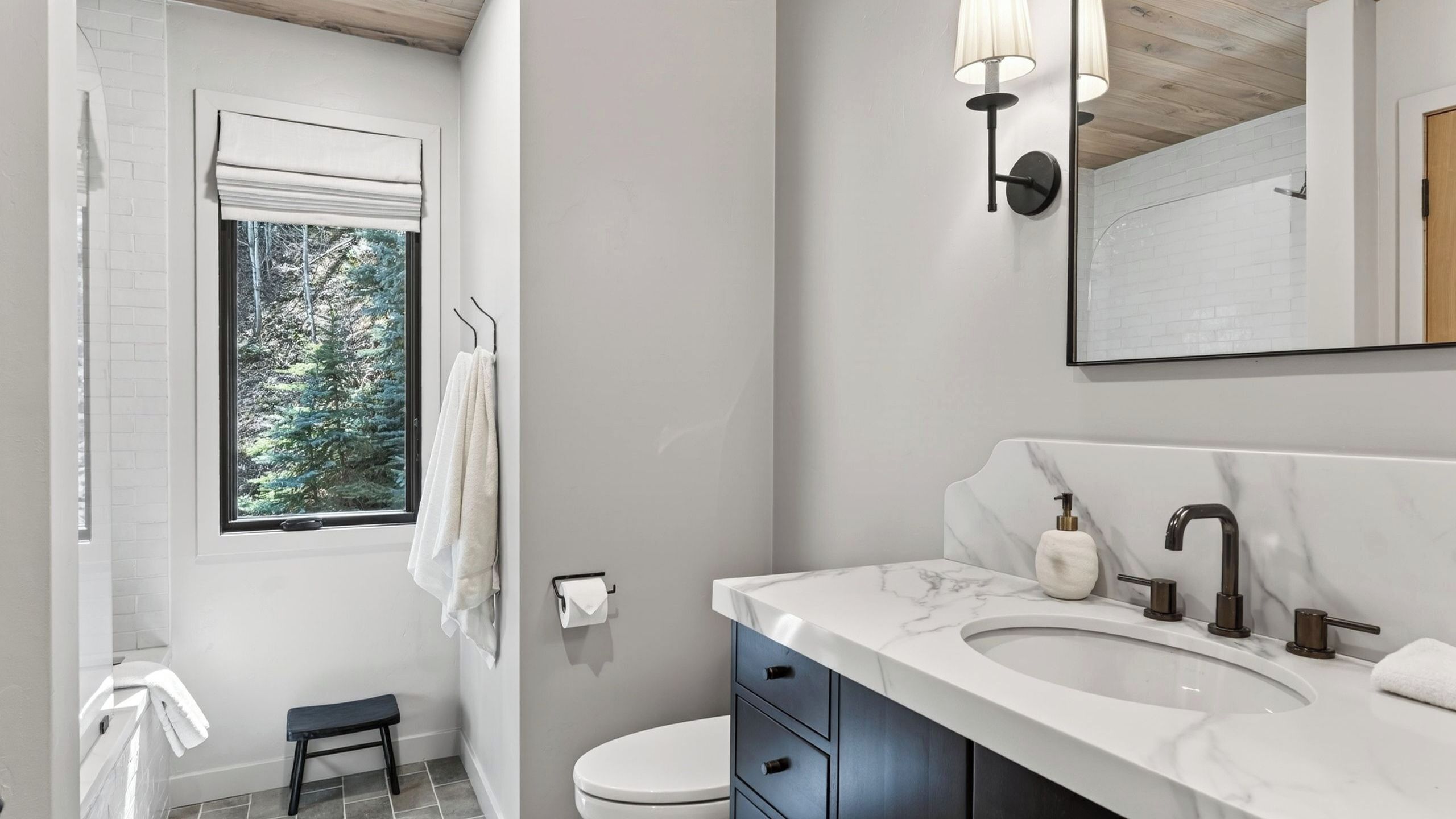 A bathroom with a white sink, marble countertop, and a window with a view of trees.
