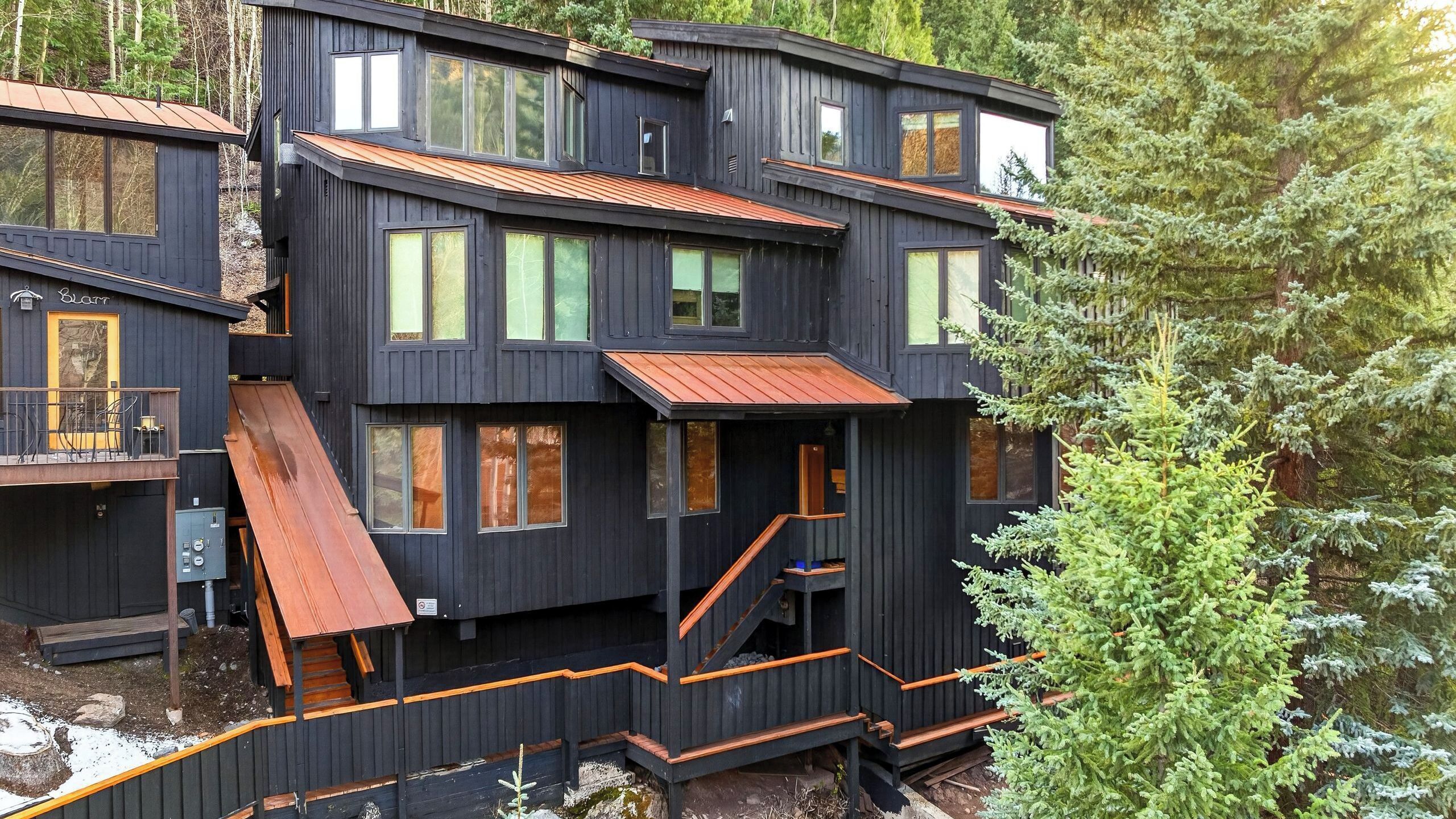 A multi-story wooden cabin with a balcony, a staircase, and a small outdoor area.