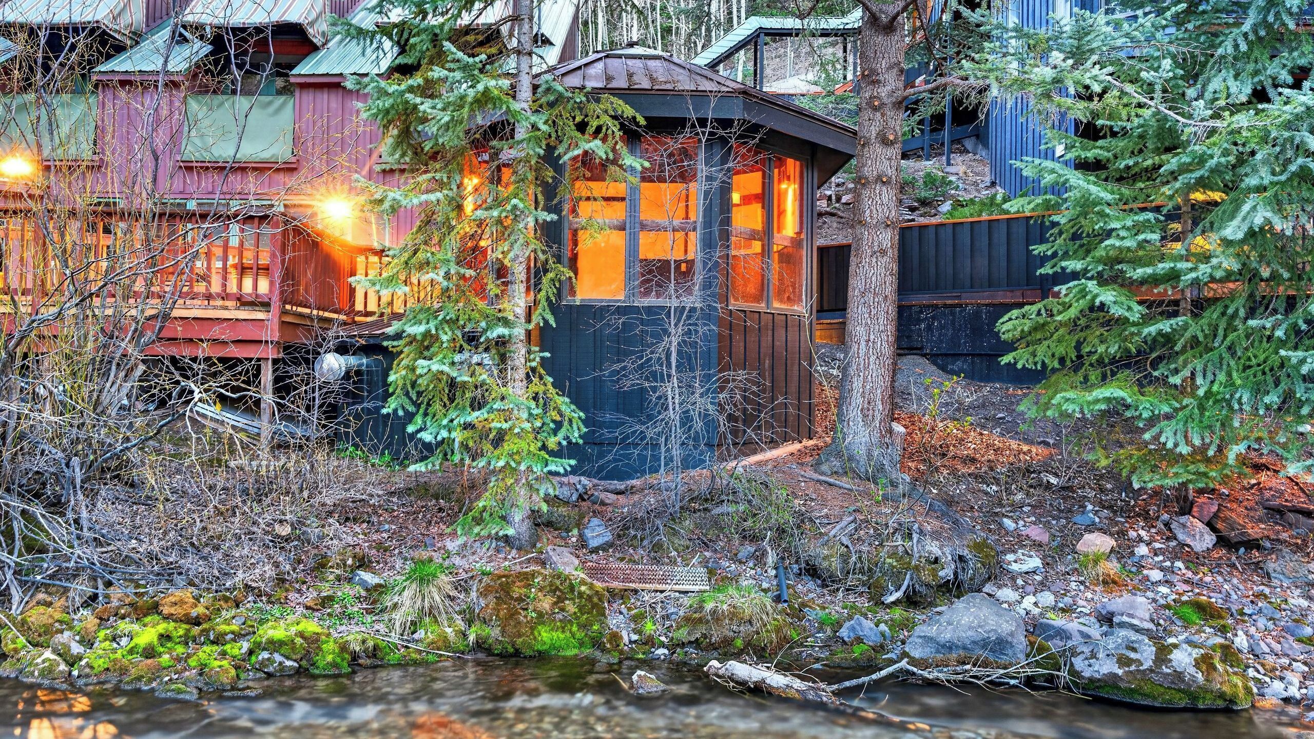 A rustic cabin with a wooden exterior, a small porch, and a stream in front.